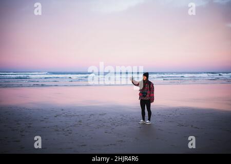 Lächelnde junge Frau, die bei Sonnenaufgang allein am Strand von Oregon Selfie gemacht hat Stockfoto