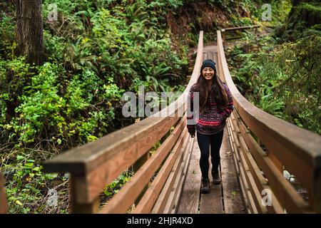 Lächelnde junge Frau überquert die Brücke auf dem Naturpfad von Oregon Stockfoto