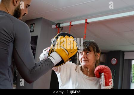 Frau im Boxtraining im Silberzeitalter wirft Schlag auf den Trainingshandschuh ihres Lehrers Stockfoto