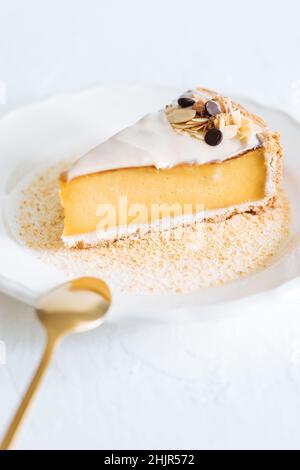 Französischer Flan auf weißem Teller mit Keksbröseln um sich herum, mit Mandeln darauf. Ein Stück Kuchen auf weißem, hellem Hintergrund, traditionelles französisches Dessert Stockfoto