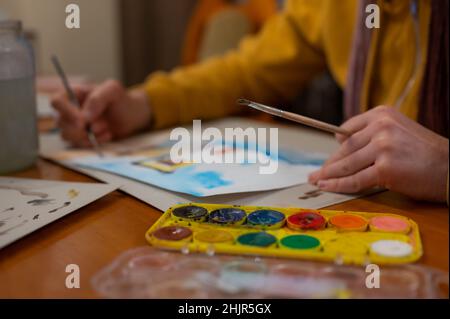 Nahaufnahme des Aquarell-Malprozesses. Pinsel in der Hand über Malerei. Bunte mittelalterliche Stadtstraße auf Papptafel. Stockfoto