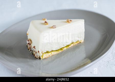 Vierlagiger Kuchen mit Pistazien, Vanille und weißer Schokolade auf grauem Teller mit Pistazien darauf Stockfoto