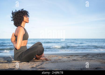 Die schwarze Frau saß entspannt am Strand und praktizierte Yoga Stockfoto