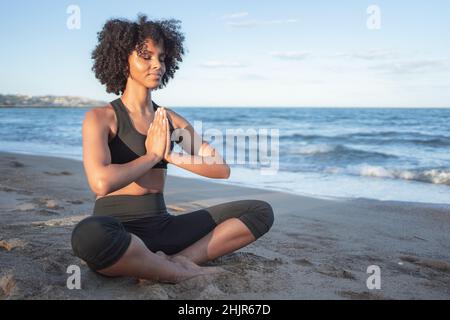 Die schwarze Frau saß entspannt am Strand und praktizierte Yoga Stockfoto