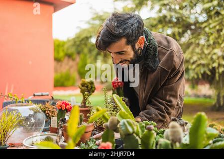 Lächelnder Gärtner, der den Zustand und das Wachstum der Pflanzen überprüft Stockfoto