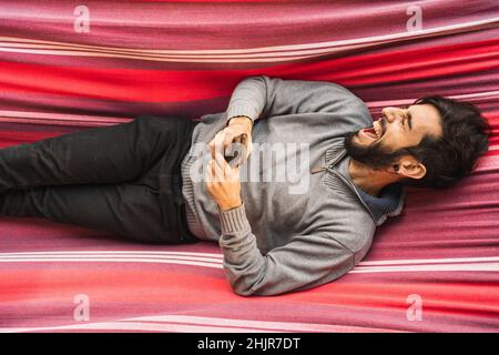 Hipster-Mann lachend mit Handy in einer Hängematte Stockfoto