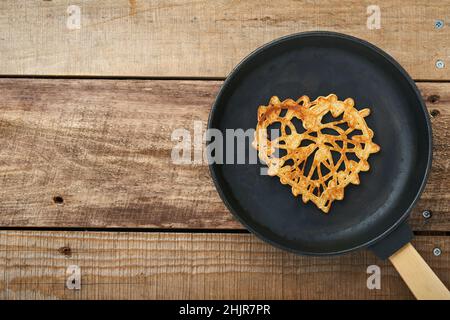 Herzförmige Spitzenpfannkuchen oder Crepes auf gusseiserner Pfanne auf altem rustikalem Holzhintergrund. Tischeinstellung für Ihr Lieblingsfrühstück am Valentinstag. T Stockfoto