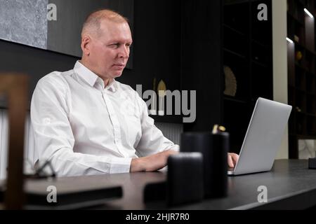 Seriös reifer Geschäftsmann in formeller Kleidung sitzt am Schreibtisch und arbeitet im Büro an einem Laptop. Online arbeiten und Computertechnik im Arbeitskonzept nutzen. Hochwertige Fotos Stockfoto