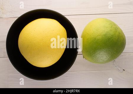 Zwei saftige Bio-Pomelos mit schwarzer Keramikplatte auf einem Holztisch, Makroaufnahme, Draufsicht. Stockfoto