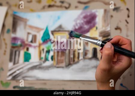 Nahaufnahme des lebendigen Aquarellmalprozesses. Pinsel in der Hand über Malerei. Bunte mittelalterliche Stadtstraße auf Papptafel. Stockfoto