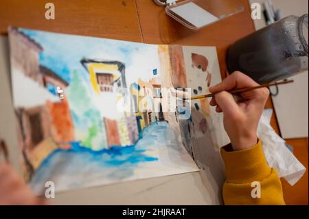 Nahaufnahme des lebendigen Aquarellmalprozesses. Pinsel in der Hand über Malerei. Bunte mittelalterliche Stadtstraße auf Papptafel. Stockfoto