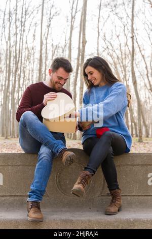 Junges Paar, das den valentinstag feiert und sich gegenseitig ein Geschenk in einem Park schenkt Stockfoto