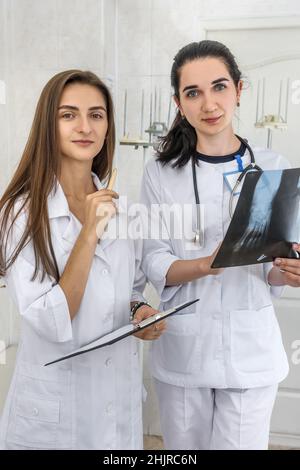 Arzt mit einem jungen Praktikanten, der die Röntgenaufnahme des Patienten im Krankenhaus analysiert. Eine Frau hält und und sie beide schauen darauf Stockfoto