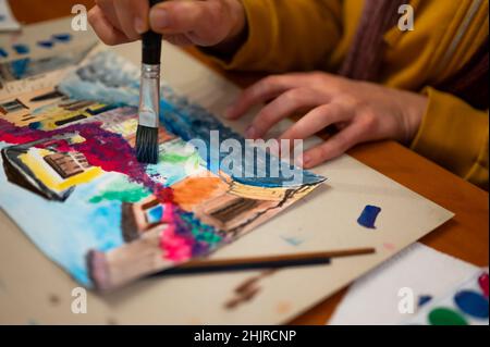 Nahaufnahme des lebendigen Aquarellmalprozesses. Pinsel in der Hand über Malerei. Bunte mittelalterliche Stadtstraße auf Papptafel. Stockfoto