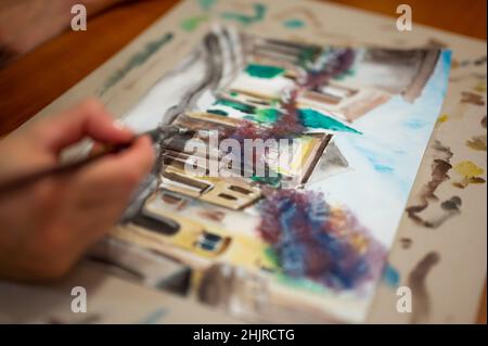 Nahaufnahme des lebendigen Aquarellmalprozesses. Pinsel in der Hand über Malerei. Bunte mittelalterliche Stadtstraße auf Papptafel. Stockfoto