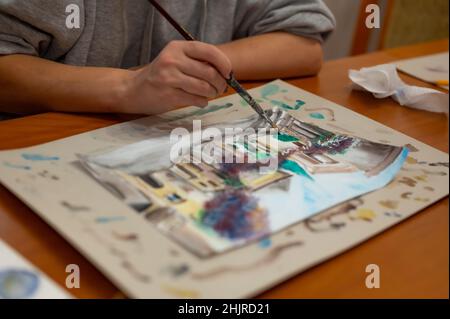 Nahaufnahme des lebendigen Aquarellmalprozesses. Pinsel in der Hand über Malerei. Bunte mittelalterliche Stadtstraße auf Papptafel. Stockfoto