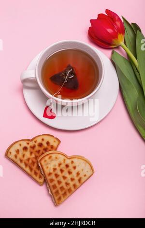 Valentinstag-Frühstück im Bett. Geschenk, Tee belgische Waffeln Blume, Herzen auf rosa Hintergrund. Valentinstag-Konzept.. Flach liegend, Draufsicht Stockfoto