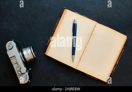 Ein altes offenes Buch mit leeren Seiten und einer Vintage-Kamera auf dunklem Hintergrund, Draufsicht, flach liegend Stockfoto