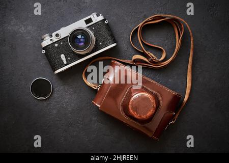 Alte schäbige Retro-Kamera und Ledertasche auf schwarzem Graphit-Hintergrund in Nahaufnahme, flach liegend Stockfoto