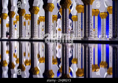 Symmetrische Poolspiegelung der monumentalen Marmorsäulen der Scheich-Zayed-Moschee in Abu Dhabi bei Nacht Stockfoto
