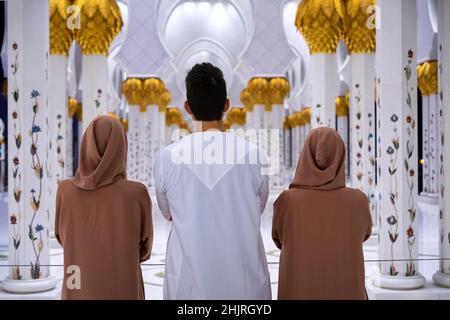 Ein Mann und zwei Frauen, die in traditioneller arabischer Kleidung mit den Armen in der Kolonnade der Großen Moschee stehen, von hinten geschossen Stockfoto