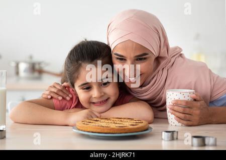 Hausgemachtes Gebäck. Glückliche Islamische Mutter Und Tochter, Die Frisch Gebackenen Kuchen Betrachten Stockfoto