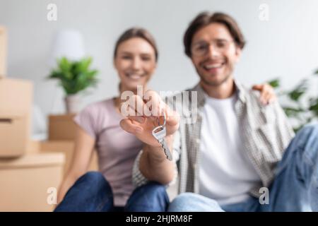 Fröhlicher junger europäischer Mann in Brille und Frau zeigt Schlüssel aus dem neuen eigenen Appartement im Zimmer Stockfoto