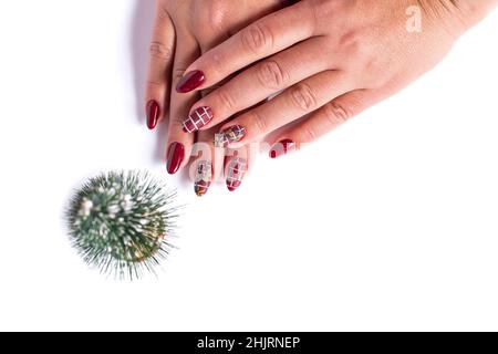 Schöne rote Maniküre auf weiblichen Händen und kleine künstliche Cristmas Baum, isoliert auf einem weißen mit Kopierraum. Stockfoto