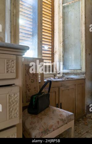 Italien, 20. Januar 2021. Schwarze Handtasche der Frau, die auf einem alten Stuhl liegt. In einem verlassenen Haus. Urbex Stockfoto