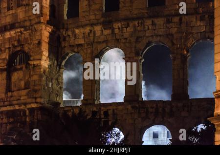 Die Pula Arena in Kroatien bei Nacht. Im antiken römischen Amphitheater findet ein Live-Konzert statt. Aus den gewölbten Steinwänden kommen Lichter und Rauch. Stockfoto