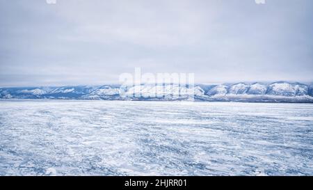 Eis des Baikalsees am frühen Morgen auf dem Hintergrund von Eis und Bergen. Stockfoto