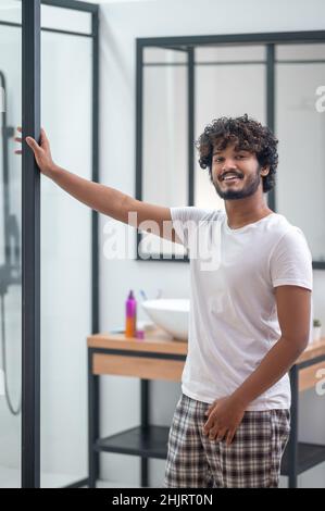 Zufriedener dunkelhaariger Kerl, der im Badezimmer steht Stockfoto