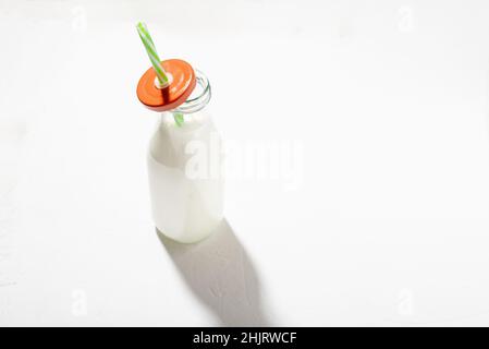 Milch in einer Flasche mit einem Strohhalm auf weißem Hintergrund. Milch oder Joghurt auf pflanzlicher Basis. Stockfoto