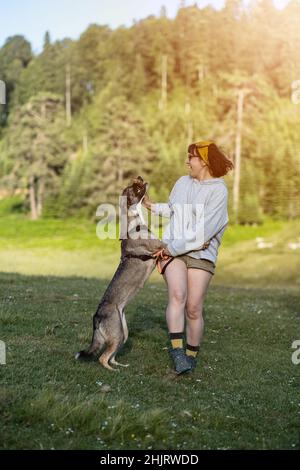 Junge Frau, die im Wald mit Hund spielt, junge kaukasische Frau, die ihren Hund trainiert Stockfoto