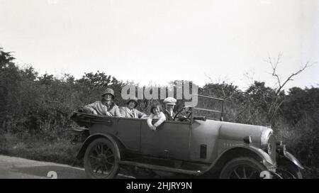 Um 1920s, historisch, auf einer Landstraße, eine Familie... Mutter, Schwester und kleine Tochter und Junge, in einer Stoffkappe, sitzend in einem offenen Wagen der Ära, England, Großbritannien. Beide Damen tragen Hüte. Auf der rechten Fahrzeugverkleidung auf der Fahrerseite ragt von unten ein Startgriff heraus und die Hupe befindet sich neben dem Lenkrad. Stockfoto