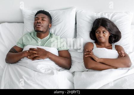 Unzufrieden unglückliche, tausendjährige afroamerikanische Frau leidet unter Lärm und Schnarchen des schlafenden Mannes im Bett Stockfoto