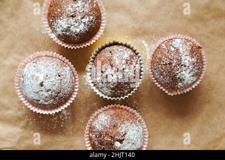 Schokoladen-Muffins mit Puderzucker auf Backpapier. Draufsicht, Food Hintergrund, flaches Lay. Stockfoto