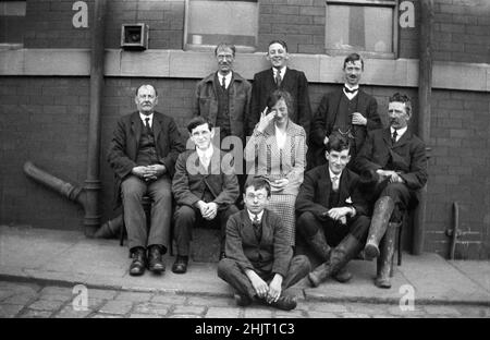 Um 1920er, historisch, Mitarbeiter von TPCG, Dudley, versammeln sich draußen auf einem Bürgersteig für ihr Foto, Warwick, England, Großbritannien. Das Bild zeigt die formelle Arbeitskleidung der Epoche, alle Männer tragen Anzüge und Krawatten. Zwei der Männer haben Uhrketten an ihrer Weste. Die einzige junge Mitarbeiterin sitzt in der Mitte und wischte sich die Augen, während sie lachte, während der junge Mann hinter ihr immer noch lachte. Der Herr mit den wellington-Stiefeln auf der rechten Seite und mit dem Heck könnte der Boss sein, da er definitiv nicht lacht! Stockfoto