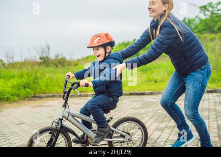 Mama lehrt Sohn ein Fahrrad im Park zu fahren Stockfoto