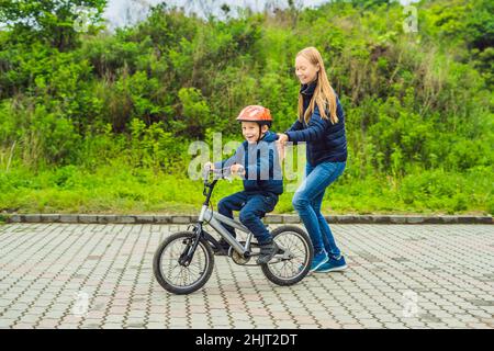 Mama lehrt Sohn ein Fahrrad im Park zu fahren Stockfoto