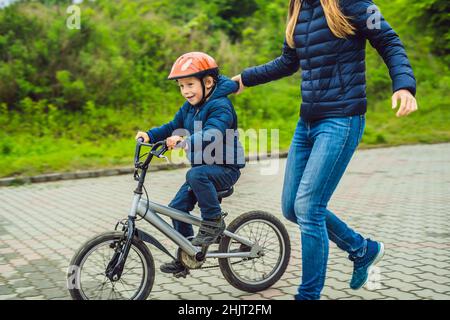 Mama lehrt Sohn ein Fahrrad im Park zu fahren Stockfoto