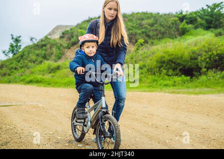 Mama lehrt Sohn ein Fahrrad im Park zu fahren Stockfoto