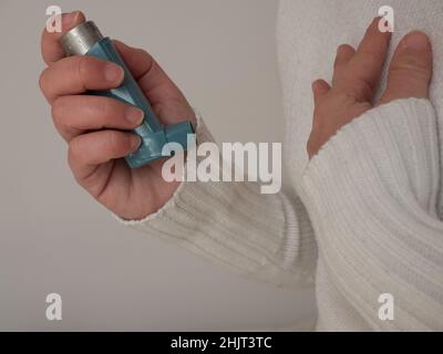 Frau mittleren Alters, die einen blauen Asthma-Inhalator verwendet, um einen Asthmaanfall zu lindern. Das pharmazeutische Produkt wird zur Vorbeugung und Behandlung von Keuchen und Kurzwerden verwendet Stockfoto