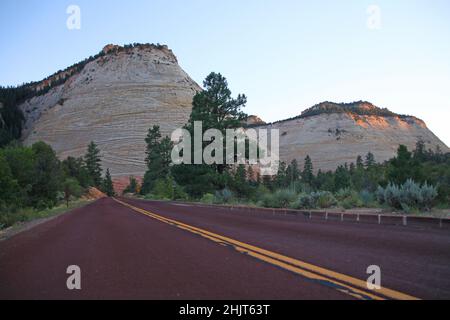 Die rote gepflasterte Straße in Richtung der weißen Checkerboard Mesa bei einem Sommeruntergang im Zion National Park in Utah Stockfoto