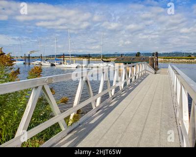 Holzbrücke mit Klipppfad an einer Uferpromenade. Perspektivischer Blick auf den hölzernen Pier am See oder Fluss. Wunderschöner Yachthafen Stockfoto