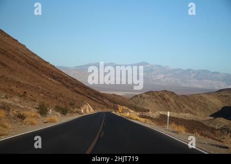 Die schwarze Asphaltstraße mit den Bergen der Linken und auf Distanz in Kalifornien Stockfoto