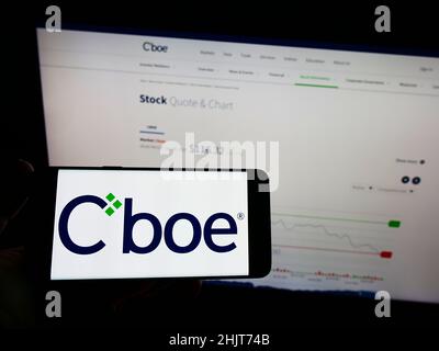 Person mit Mobiltelefon und Logo des US-Finanzunternehmens CBOE Global Markets Inc. Auf dem Bildschirm vor der Webseite. Konzentrieren Sie sich auf die Telefonanzeige. Stockfoto