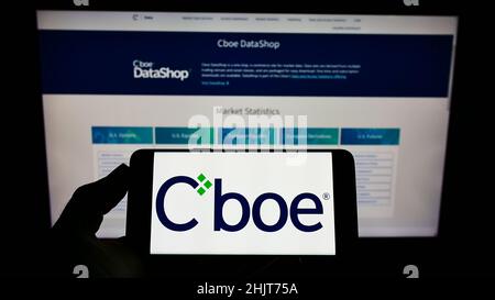 Person mit Mobiltelefon und Logo des amerikanischen Finanzunternehmens CBOE Global Markets Inc. Auf dem Bildschirm vor der Webseite. Konzentrieren Sie sich auf die Telefonanzeige. Stockfoto