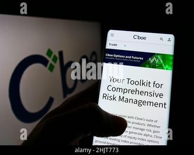 Person mit Mobiltelefon und Webseite des US-Finanzunternehmens CBOE Global Markets Inc. Auf dem Bildschirm mit Logo. Konzentrieren Sie sich auf die Mitte des Telefondisplays. Stockfoto