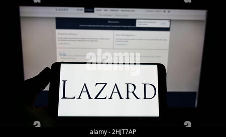 Person, die Mobiltelefon mit dem Logo des amerikanischen Finanzdienstleisters Lazard Ltd. Auf dem Bildschirm vor der Webseite hält. Konzentrieren Sie sich auf die Telefonanzeige. Stockfoto